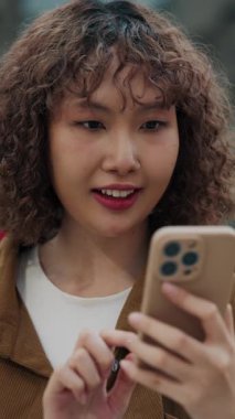 Dikey video. Neşeli Kız dışarıda telefonda galibiyetinin tadını çıkarıyor. Genç mutlu bayan Smartphone 'da güzel haberler alıyor, heyecanlanıyor. Halk ve Teknoloji Konsepti