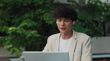 Keyifli esmer girişimci portresi sokak kafesinde laptopla ortaklarla görüntülü sohbete katılıyor. Kulaklıklı profesyonel bir işadamı çevrimiçi toplantıda meslektaşlarıyla konuşuyor.