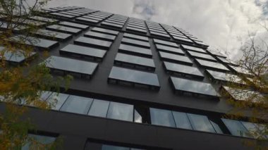 Gökyüzü alçak açılı bulutlara karşı minimalist siyah cepheli kampüs kulesi gökdeleni projesi. Şehir merkezindeki lüks iş merkezi ticari gayrimenkul.