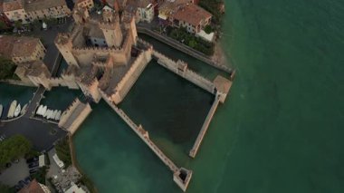 Sirmione, Lombardy, İtalya 'daki Scaliger Kalesi' nin dikey görüntüsü. Garda Gölü 'nün zümrüt suyuyla çevrili güçlendirilmiş yapı, ortaçağ duvarları ve tekne iskelesini gösteriyor.