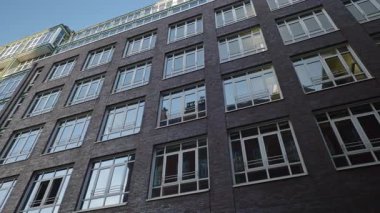 Eski şehrin alçak açılı çekimlerinde kare pencereli ofis binası cephesini kaydır. Anıt, kentteki tuğla dışavurumculuğunu tasvir ediyor