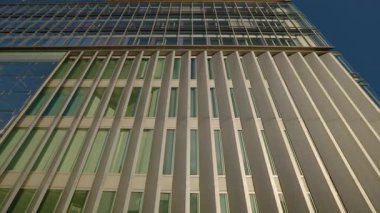 Mavi gökyüzü alçak açılı çekimde ön cephesinde panjurları olan yüksek bir ofis binası. Şehir merkezindeki modern kentsel iş mimarisinin şık tasarımı