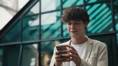 Dışarıdaki ticari binalara karşı akıllı telefondan mesaj atan bir adamın portresi. Genç işadamı, döviz kurlarını caddedeki mobil uygulamalarla kontrol ediyor. Gençler için başarılı bir kariyer