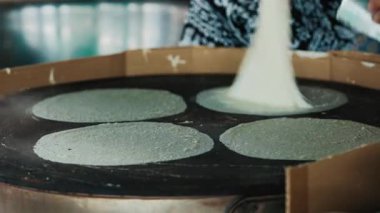 Geleneksel bir Tayland sokak yiyecek pazarında sıcak ızgarada ince krep yapmak için hamur işi yapan bir satıcının yakın çekimi. Tayland 'da otantik yerel pişirme süreci.