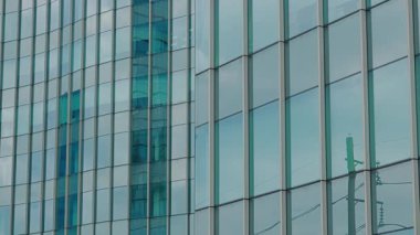 Modern bir ofis binasının panoramik manzarası. Çağdaş bir iş bölgesinde yansıtıcı cam cepheli. Sokak seviyesinden çekilen dikey çizgiler ve simetri vurgulanıyor.