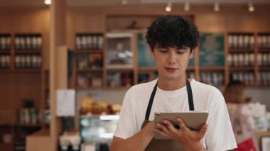 Kafede tablet bilgisayarla sipariş veren özenli erkek sunucunun portresi. Genç adam restoranda misafirlerle çalışırken dijital menü kullanır. Pozitif erkek kafeteryası çalışanı