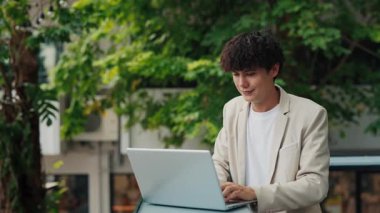 Şehir merkezinde dizüstü bilgisayarda çalışan kıvırcık saçlı girişimcinin portresi. Genç işadamı kafede bilgisayarda rapor hazırlıyor. Müdür Freelancer iş için çevrimiçi hizmetleri kullanır