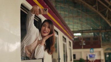 Yolcu arabasının camından sarkan cep telefonuyla selfie çeken Asyalı gururlu kadının portresi. Neşeli kadın gezgin, tren istasyonunda seyahat blogu için fotoğraf çekiyor. Boşluğu kopyala
