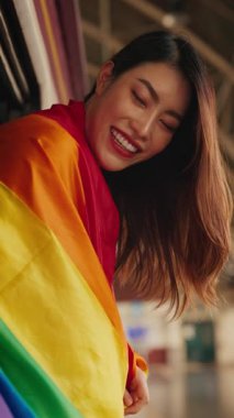 Demiryolu arabasının camından bakan gülümseyen ve gökkuşağı bayraklı mutlu Asyalı kadın portresi. Esmer lezbiyen turist, LGBT gururlu ay trenini destekliyor. Dikey çekim