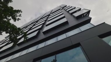 Bulutlu gökyüzü alçak açılı çekimin altında dekore edilmiş siyah cepheli kampüs binası projesi. Şehir merkezindeki yenilikçi iş merkezi mimari simgesi