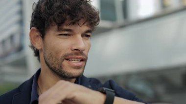 Pozitif İspanyol iş adamının portresi akıllı adımlarla konuşuyor ve sokakta yakın plan çekimde duruyor. Latin girişimci şirket binasındaki müşteriyi aramak için dijital kol saati kullanıyor