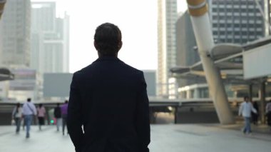 İş adamı şehir meydanında modern şehir merkezinin arka planında yürüyor. Şirketin CEO 'su genç adam megapolis' in zarif mimari formlarını gözlemliyor. İş başarısı