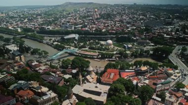 TBILISI, GEORGIA - 17 Haziran 2024: Gürcistan 'da güneşli bir günde Barış Köprüsü, Rike Parkı ve Kutsal Üçlü Katedrali de dahil olmak üzere Tiflis tarihi ve modern simgelerinin insansız hava aracı görüntüsü