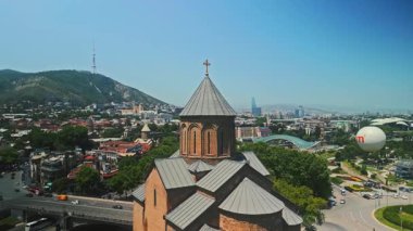 TBILISI, GEORGIA - 15 Ocak 2023: Tiflis 'teki tarihi kilisenin insansız hava aracı görüntüsü, panoramik şehir manzarası, modern binalar ve arka planda Mtatsminda tepesi. Gürcistan başkentinin havadan silueti