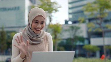 Malezyalı mutlu iş kadını portresi şehir merkezinde dizüstü bilgisayarla cevap veriyor. Neşeli Muslin hanım şehir parkında bilgisayarla arkadaşlarıyla konuşuyor.