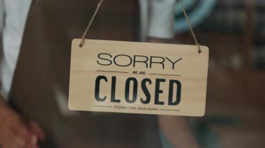 Cam kafe kapısında, sunucu ellerinin tabela çevirme görüntüsü kapatıldı. Önlüklü restoran garsonu, müşterileri masa kullanarak kahve dükkanına davet ediyor. Yiyecek ve içecek dükkanı açmak