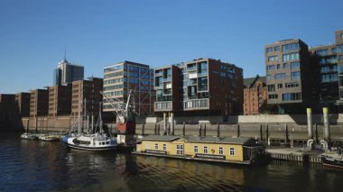 HAMBURG, GERMANY - 23 Eylül 2024: Elbe nehir limanındaki vinç ve gemi yakınlarındaki eski yüzen otel ve deniz kenarındaki binalara karşı. Apartman bölgesi ve açık gökyüzü altında limanı olan modern şehir manzarası