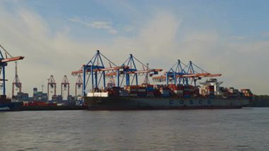 HAMBURG, Almanya - 23 Eylül 2024: Gantry vinçleri Elbe Nehri 'ndeki kargo gemisine konteyner yüklüyor. Modern makineler, güzel bir günde limandaki tersanedeki gemi gemisine yük yerleştirirler.