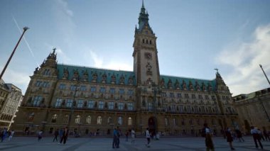 HAMBURG, ALMANY - 23 Eylül 2024: saat kulesiyle belediye binası ve açık bulutlu gökyüzüne karşı Cyan çatısı. Turistler eski kentteki meydanda yürüyen mimari simgeleri ziyaret ediyorlar. Avrupa tatili