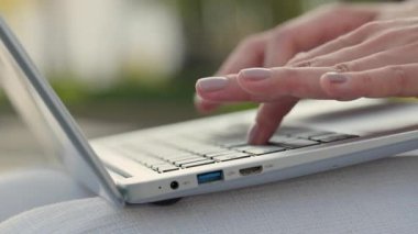 Kadın ellerinin yakın çekim görüntüsü dizüstü bilgisayarda yazacak ve şehir parkında makale yazacak. Kadın blogcu, yaz kenti bahçesinde oturan taşınabilir bilgisayar aracılığıyla takipçileriyle çevrimiçi iletişim kuruyor