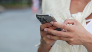 Kadın eli görüntüsü şehrin arka planında akıllı telefondan çevrimiçi mesaj atıyor. Bayan cep telefonuyla mesajlar yolluyor ve sokak kapanışında duruyor. Haberleşme servisi.