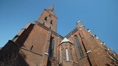HAMBURG, Almanya - 23 Eylül 2024: Mavi gökyüzüne karşı yüksek kulesi olan Aziz Peter Kilisesi en eski Hıristiyan tapınağı. Kasaba bölgesinde eski bir dini tuğla bina alçak açılı çekim
