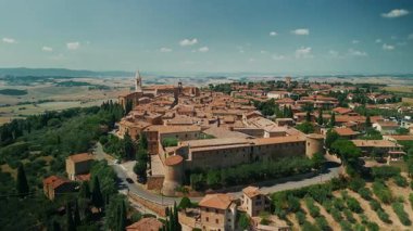 Pienza, İtalya: 27 Ağustos 2024: Tepe üzerindeki tüm Pienza kasabasının panoramik hava manzarası, kırmızı kiremitli çatıları ve zeytin ağaçları ve üzüm bağları arasında yuva yapmış taş kuleleri.