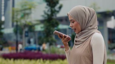 Genç Malezyalı tesettürcü kadın portresi şehirdeki akıllı telefon yürüyüşlerinde ses masajı kayıtları tutuyor. Şehir merkezinde Müslüman kadınlar ellerini kullanmadan telefonla konuşuyor.
