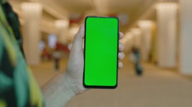 Yeşil ekranlı akıllı telefonu olan bir erkek alışveriş merkezinde taklit ediyor. Cep telefonu kroma anahtar ekranını kapat. İş uygulaması için modern aygıt boş ekran şablonu, sosyal medya