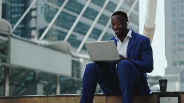 Mutlu Afrikalı Amerikalı menajerin portresi şehir ortamında dizüstü bilgisayarda görüntülere katılıyor. Keyifli iş adamı şehir merkezinde oturan müşteriyle konuşuyor. Haberleşme.