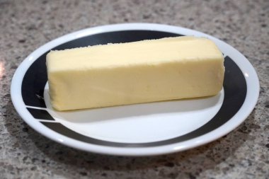 Stick of yellow butter on a black and white plate and with the stick of butter unsliced