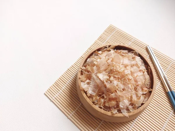 Katsuobushi. It is preserved food made from skipjack tuna. shaved like wood shavings for the broth. basis of Japanese cuisine, sprinkled on top of food as a flavoring. eaten as a side dish with rice