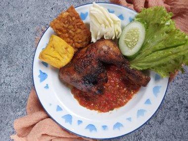 Indonesian grilled chicken. Completed with traditional chili sauce, fried tempeh and tofu, cucumber, lettice, cabbage. Isolated background