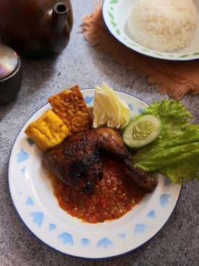 Indonesian grilled chicken. Completed with traditional chili sauce, fried tempeh and tofu, cucumber, lettice, cabbage. Isolated background