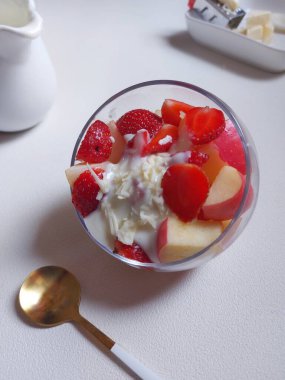 Şeffaf camda meyveler dilimlenmiş. Salata sosu ve peynirle birlikte. Meyve salatası hazırlığı. Zevkli. Tatlı ve sağlıklı yiyecekler. İzole edilmiş arkaplan beyaz