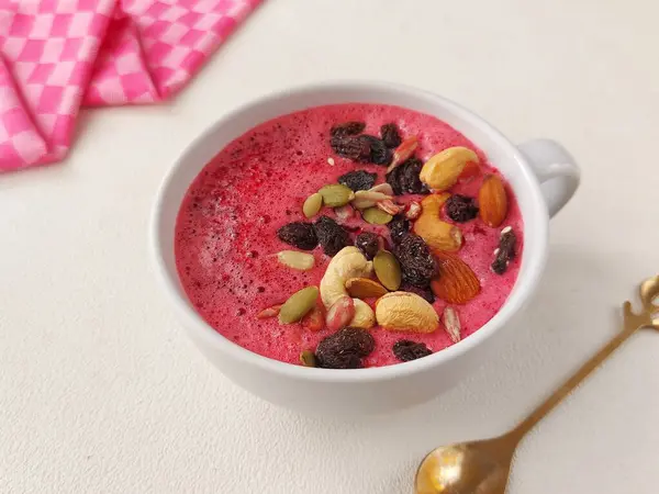 A bowl of trail mix smoothie. Made from  beetroot, pineapple and strawberry juice. Topped with dried fruit and nuts. Healthy food concept. Isolated background in white