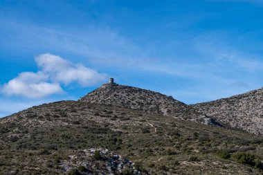 Mavi gökyüzünün altındaki dağlarda eski bir taş kulenin dikey açısı.
