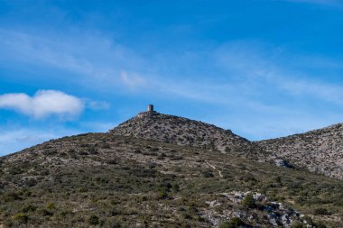 İspanya 'daki bulutlu mavi gökyüzünün altında yeşil bir arazinin ortasındaki kayalık bir dağın dikey görüntüsü.