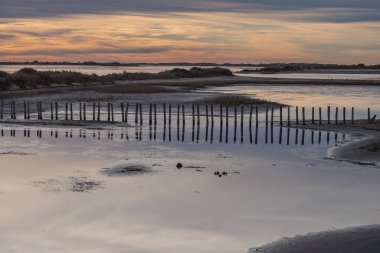 Sahilde gün batımı beyaz bir kum ve arkasında küçük bir köprü