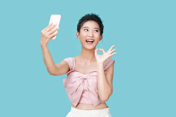 亚洲女人在青色背景下在孤立的手机上笑着拍自拍照的照片 — 图库照片
