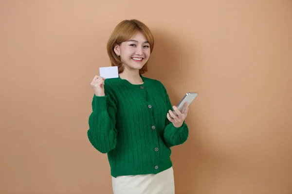 stock image Smile happily Asian woman holding smartphone and credit card shopping online on beige background.