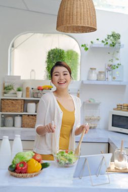 Genç Asyalı kadın mutfağında salata için sebze hazırlıyor.