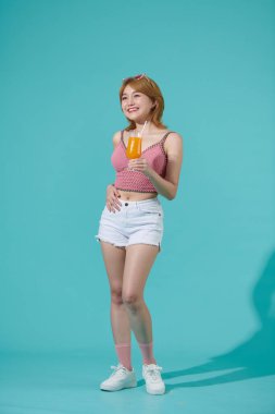 Sağlıklı gülümseyen kadın elinde portakal suyuyla bardağı tutuyor, turkuaz arka planda izole edilmiş.