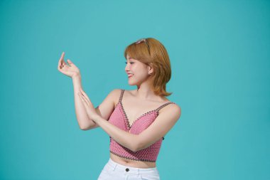 Cyan arka planda dururken kollarına dokunan gülümseyen kadın.