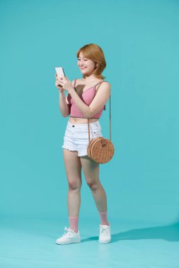 Tam boy profil fotoğrafı mutlu mutlu gülüşler cep telefonu yürüyüşü turkuaz renkli arka plan üzerinde izole edilmiş.