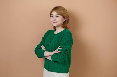 Bej arka planda kollarını kavuşturmuş kendinden emin genç bir kadının portresi.