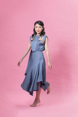 Young woman in blue dress and high heels is walking on pink background
