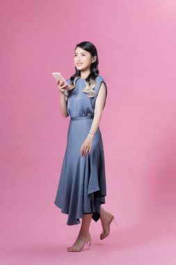 Pembe arka planda cep telefonuyla yürüyen rahatlamış genç bir kadının tüm vücudu.