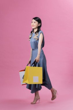 Happy beautiful woman holding many colorful shopping bags isolated on pink background