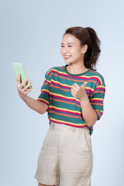 Asyalı genç bir kadın akıllı telefonuyla mesajlaşıyor, gülümsüyor ve gülümsüyor.